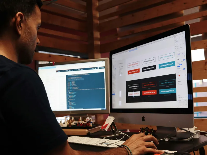 Web developer working on website design and code using two computer monitors.
