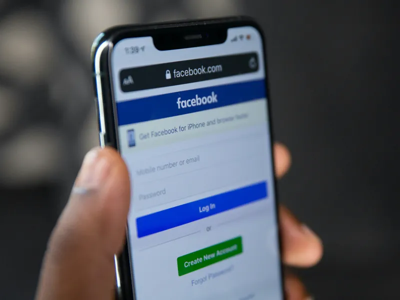 Person holding a smartphone displaying the Facebook login page on the mobile browser, showing fields for email and password entry.
